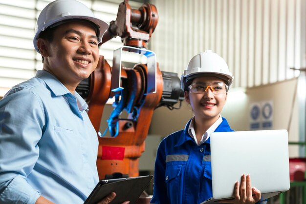 Engineer cooperation Two asian male and female technician maintenance inspect relay robot system with tablet laptop to control quality operate process work heavy industry 40 manufacturing factory