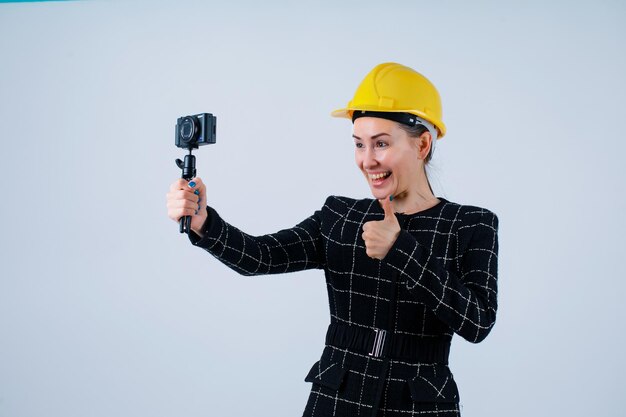 Engineer girl is taking selfie with her camera by showing perfect gesture on white background