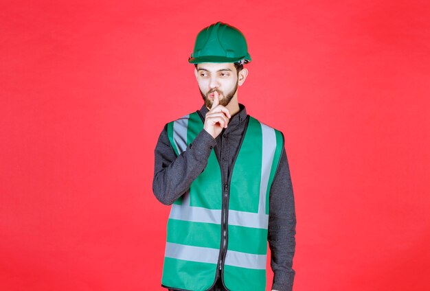 Engineer in green uniform and helmet asking for silence. 