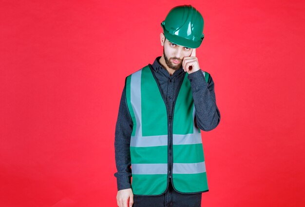 Engineer in green uniform and helmet thinking and planning. 