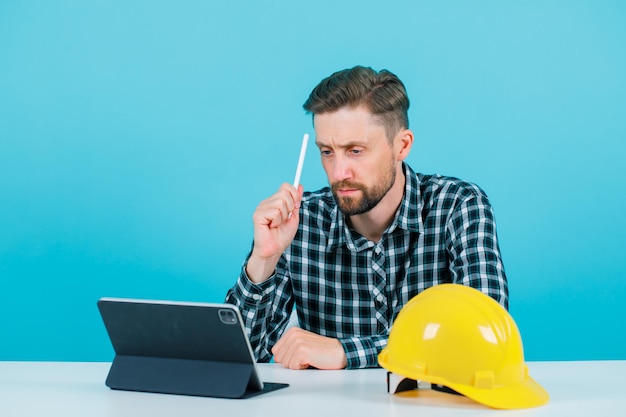 Engineer man is looking at his tablet by holding pencil on blue background