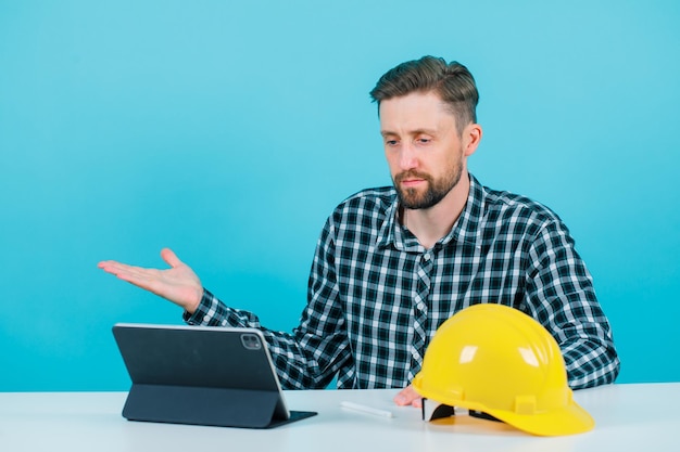 Engineer man is looking at tablet screen by raising up his left hand on blue background