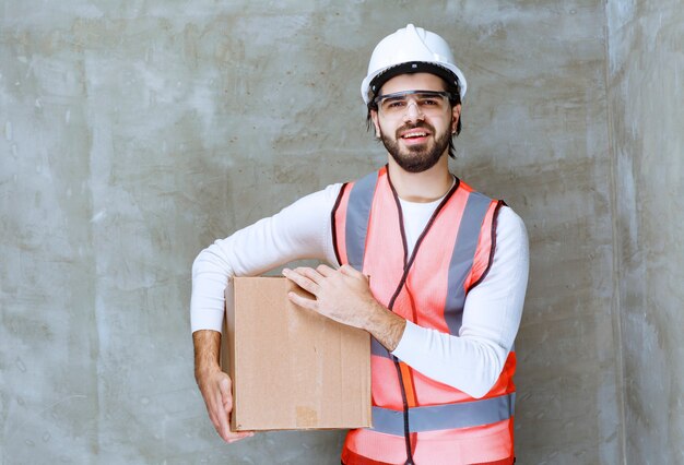 Инженер человек в белом шлеме и защитных очках, держа картонный пакет.