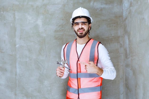 Uomo dell'ingegnere in casco bianco e occhiali protettivi che tengono chiavi metalliche.