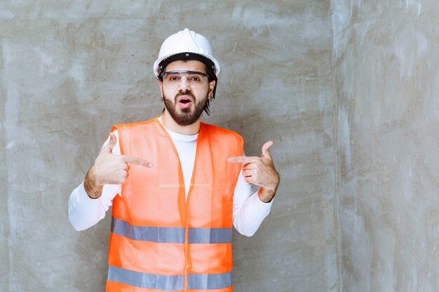 白いヘルメットと保護眼鏡を身に着けたエンジニアの男が自分を指しています。