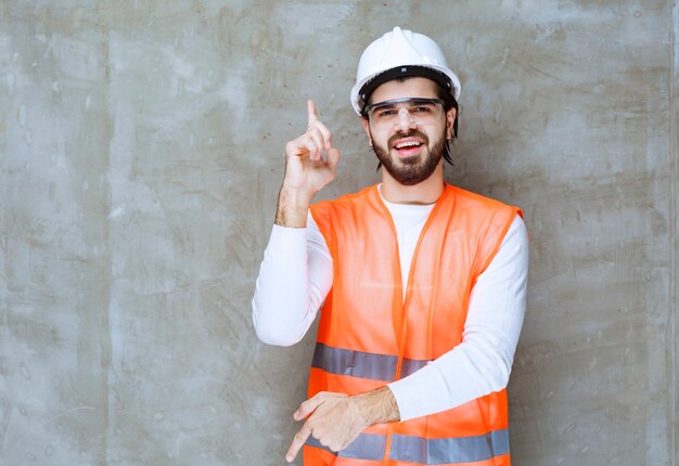 Инженер человек в белом шлеме и защитных очках, указывая вверх и вниз.