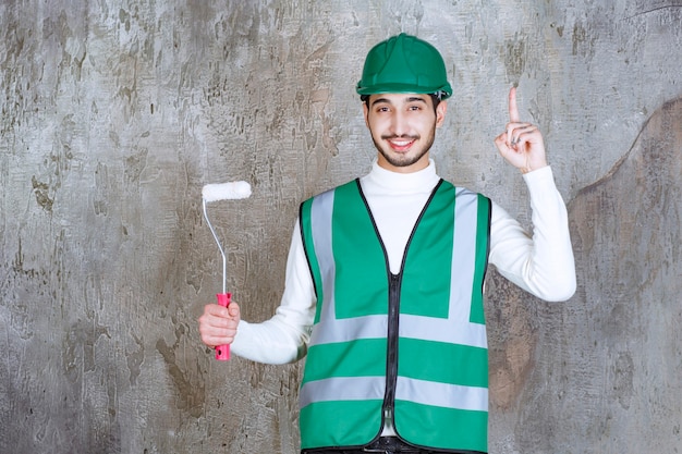 Foto gratuita ingegnere in uniforme gialla e casco che tiene un rullo di rivestimento per la pittura murale e sembra premuroso