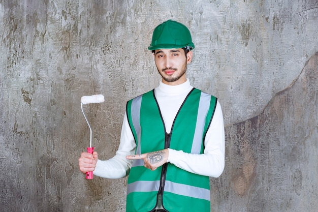 Uomo dell'ingegnere in uniforme gialla e casco che tiene un rullo di rifinitura per pittura murale.