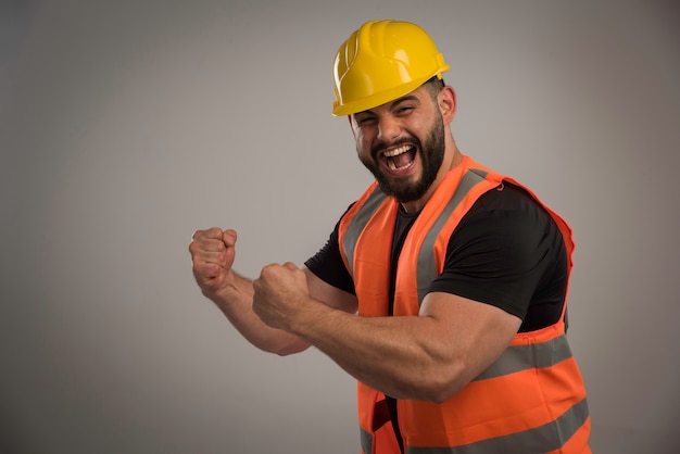 Ingegnere in uniforme arancione e casco giallo con grandi muscoli.