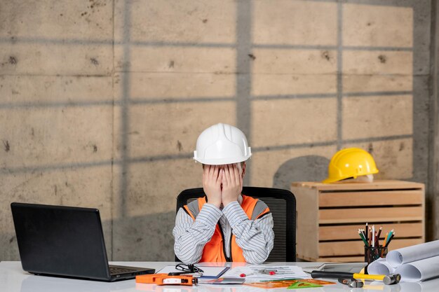 Engineer smart young cute blonde girl civil worker in helmet and vest covering face