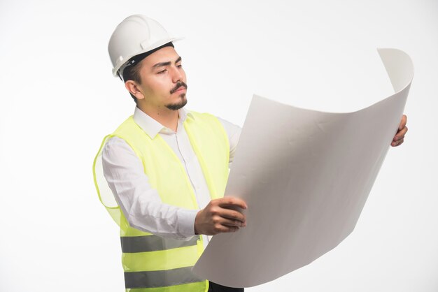 Инженер в униформе держит и читает архитектурный план постройки.