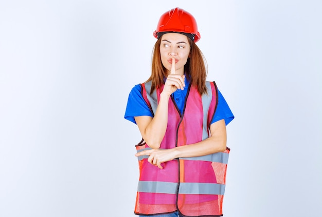 Engineer woman in uniform and red helmet asking for silence. 