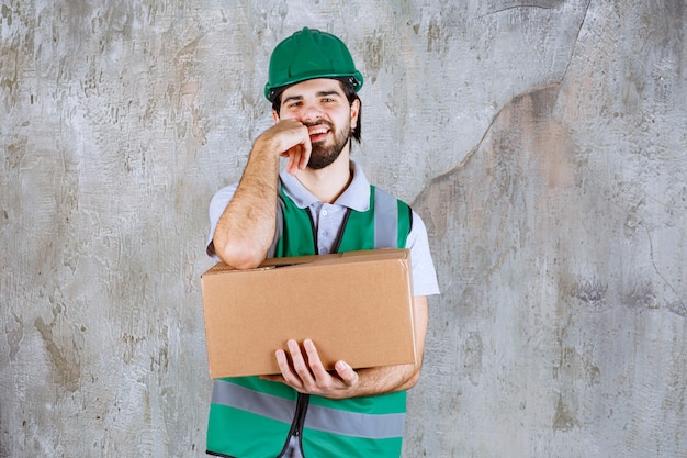 Engineer in yellow gear and helmet holding a cardboard box and looks confused and thoughtful.