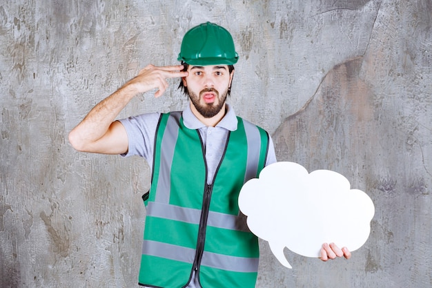 Engineer in yellow gear and helmet holding a cloud shape info board and looks thoughtful and confused.