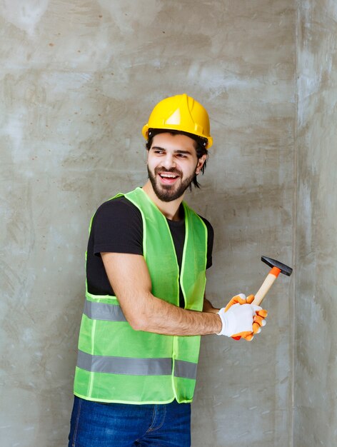 Engineer in yellow helmet and industrial gloves hitting the concrete wall with an ax