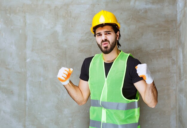 Engineer in yellow helmet and industrial gloves showing satisfaction sign