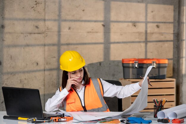 Engineer young cute smart brunette girl civil worker in helmet and vest Creating project