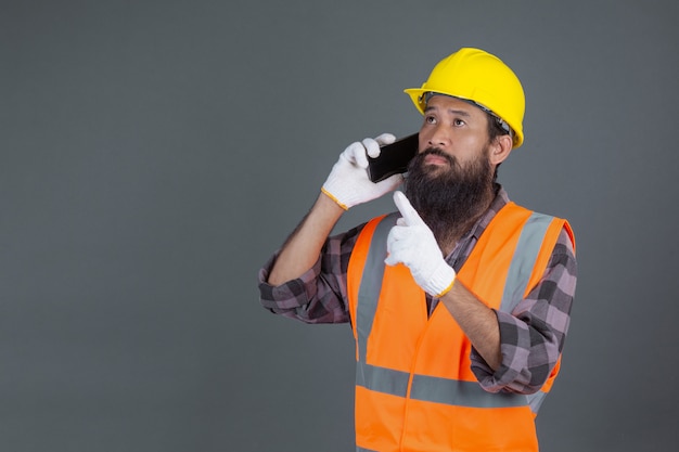 An engineering man wearing a yellow helmet holding a phone on a gray .