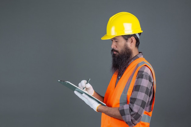 Человек инженерства нося желтый шлем с дизайном на сером цвете.