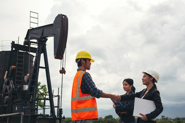 The engineering team stands beside working oil pumps with a sky .