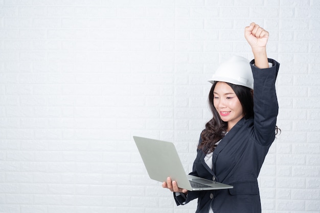 Engineering woman holding a separate notebook, white brick wall Made gestures with sign language.