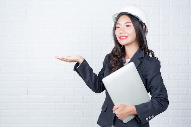 Engineering woman holding a separate notebook, white brick wall Made gestures with sign language.