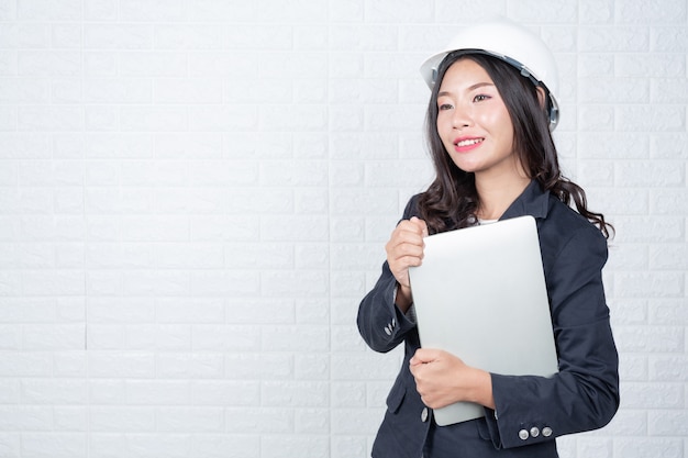 Free Photo engineering woman holding a separate notebook, white brick wall made gestures with sign language.
