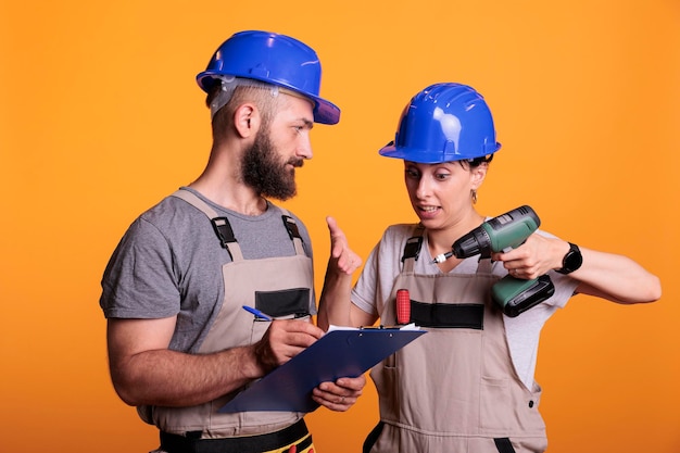 Free photo engineers team looking at construction measurements on clipboard files, holding papers and power drill gun. contractors talking about renovating project, preparing to work on refurbishment.