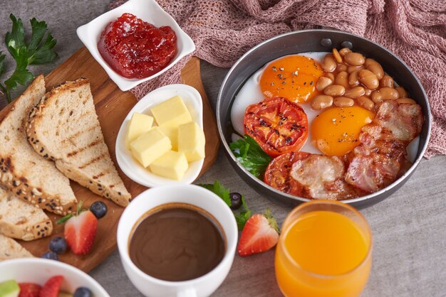 English breakfast in cooking pan with fried eggs, bacon, beans, grilled tomatoes.