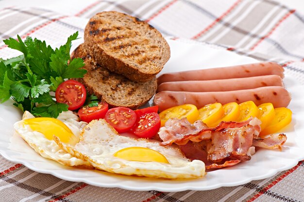 English breakfast - fried eggs, bacon, sausages and toasted rye bread