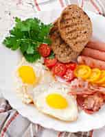 Free photo english breakfast - fried eggs, bacon, sausages and toasted rye bread