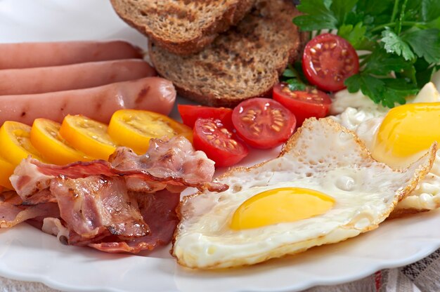 English breakfast - fried eggs, bacon, sausages and toasted rye bread