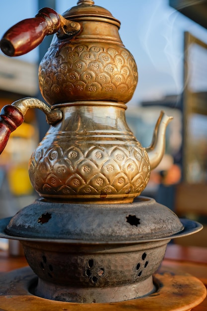 Бесплатное фото Гравированный медный турецкий чайник, селективный фокус, традиционный турецкий чайник с двойными чайниками на подставке с углями в кафе, вертикальный пар, поднимающийся из носика чайника
