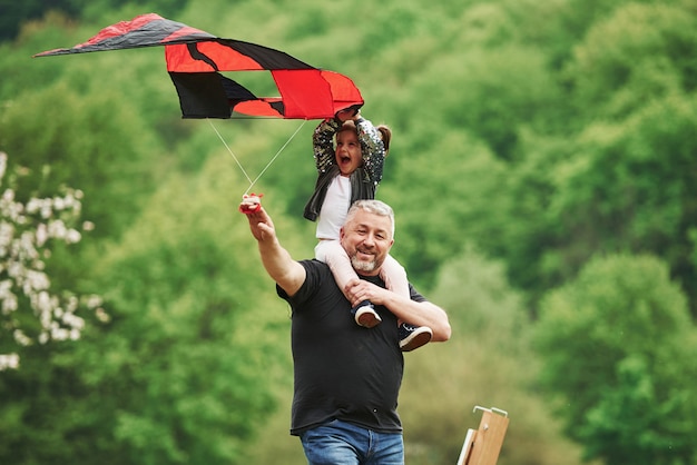 Enjoy the moment. Running with red kite. Child sitting on the man's shoulders. Having fun