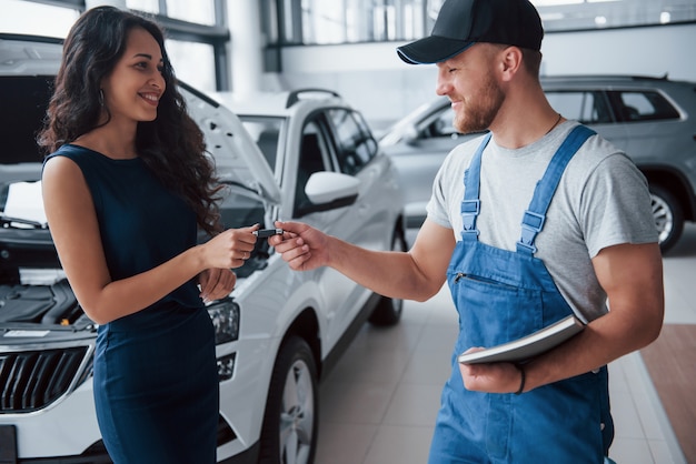 Enjoy your ride. Woman in the auto salon with employee in blue uniform taking her repaired car back