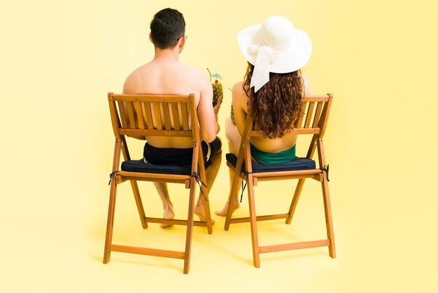 Enjoying a beautiful view on vacations. Rear view of a beautiful couple looking at the sunset at the beach while sitting on chairs and enjoying cocktails