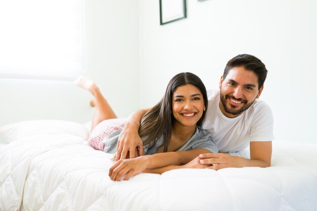 Enjoying leisure time together. Attractive boyfriend and girlfriend smiling and feeling happy while relaxing in the bedroom