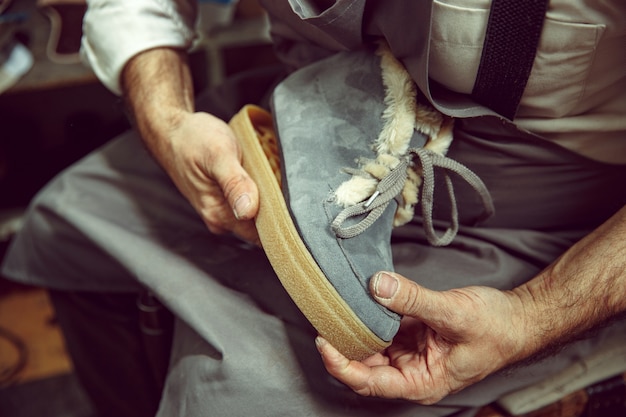 Enjoying process of creation custom made shoes. Workplace of shoe designer. Hands of shoemaker dealing with cobbler tool, close up