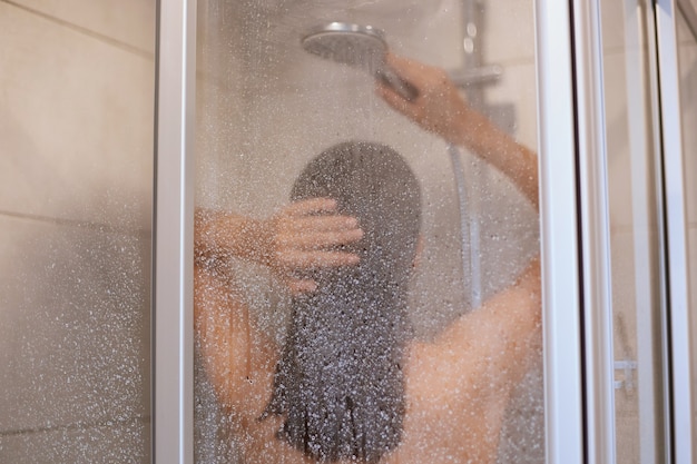 Free photo enjoying a shower. back view of beautiful young slim shirtless woman taking shower, washing hair in bathroom, hygiene, healthy and beauty, indoor shot.