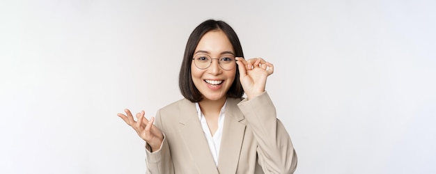 Enthusiastic asian saleswoman in glasses smiling and laughing looking amazed at camera standing in b