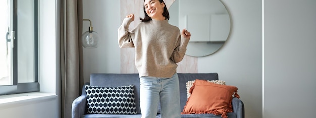 Free photo enthusiastic asian woman dancing feeling free and upbeat at her home enjoying happy day staying