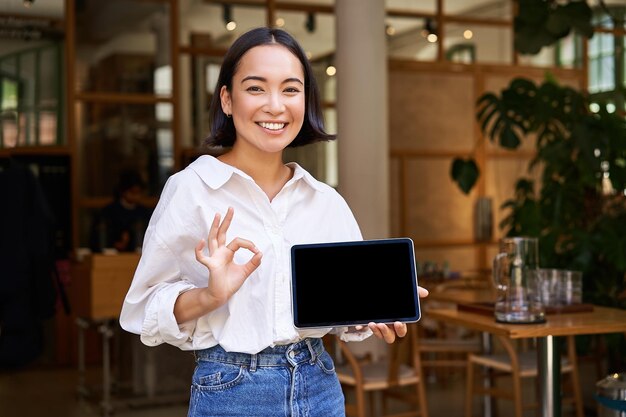 Free Photo enthusiastic asian woman shows okay sign tablet screen looks impressed recommends smth