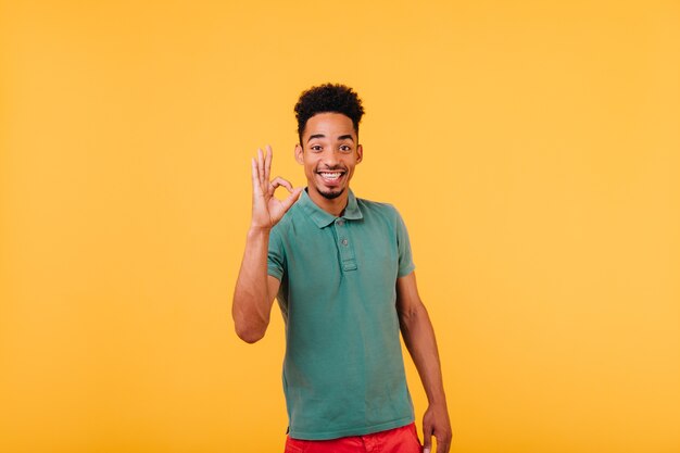 Enthusiastic black guy with short hair expressing positive emotions. Indoor shot of blissful african man enjoying.