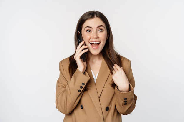 Восторженная деловая женщина разговаривает по мобильному телефону, удивленно реагирует и рада звонку, получает отличные новости, стоит на белом фоне