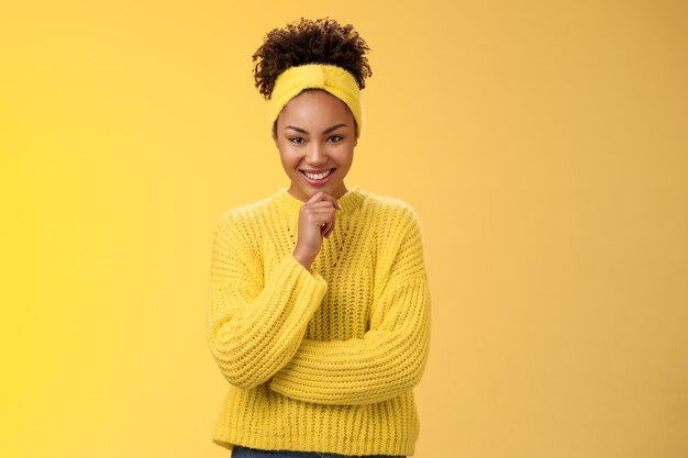 Enthusiastic creative good-looking black young woman wearing sweater headband excellent plan smiling satisfied thrilled look thoughtful camera make up idea, standing yellow background.