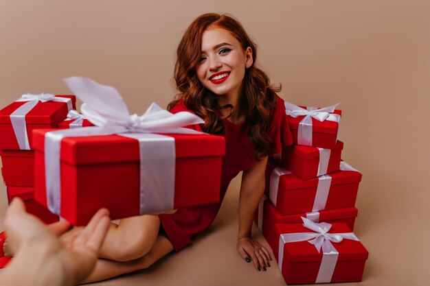 Enthusiastic curly white woman looking at birthday presents with smile Sensual ginger girl having fun in christmas