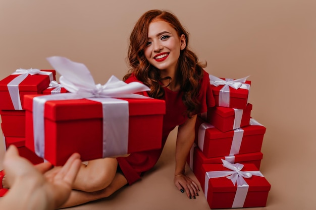 생일을 바라보는 열정적인 곱슬머리 백인 여성이 미소로 선물을 주고 있습니다. 관능적인 생강 소녀는 크리스마스에 즐거운 시간을 보내고 있습니다.