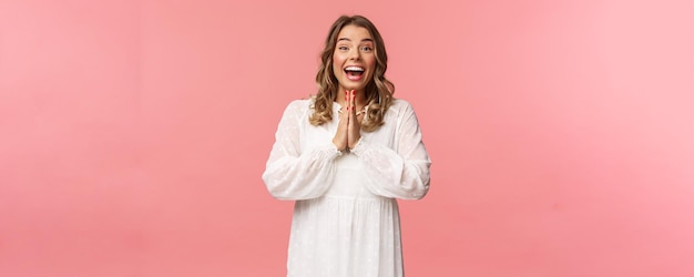 Enthusiastic and excited happy emotive blond girl applause clasping hands in thrill and amazement as seeing something really wonderful and cool smiling as dream came true pink background