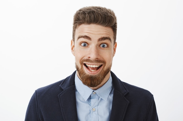 Enthusiastic excited and surprised happy handsome man with beard and deep blue eyes smiling broadly from amazement popping eyes delighted feeling impressed and astonished with good news