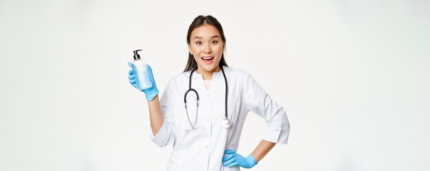 Enthusiastic female doctor in uniform showing hand soap sanitizer covid19 prevention standing over white background